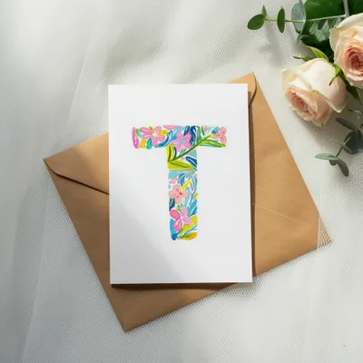 White card with floral alphabet "T" on brown envelope, with roses and eucalyptus.