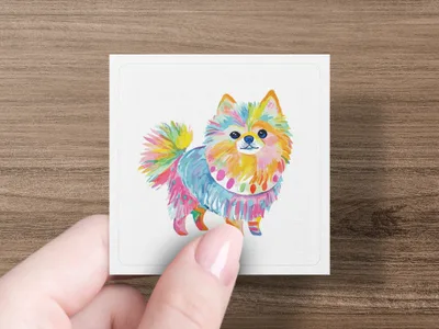 Hand holding colorful, painted Pomeranian dog artwork on white card.