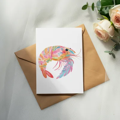 Colorful watercolor shrimp illustration on a card over a brown envelope.
