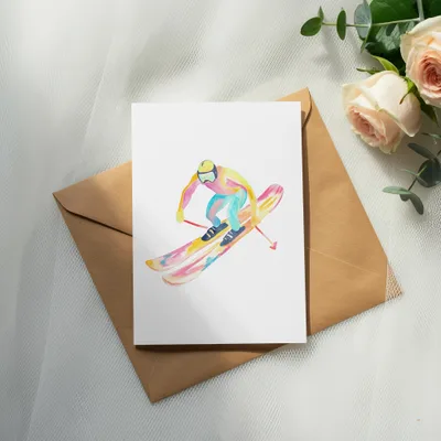 Watercolor illustration of a skier on a white card, resting on a brown envelope.