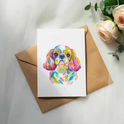 Watercolor painting of a colorful Cavalier King Charles Spaniel on a card.