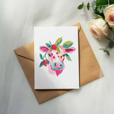 Watercolor painting of a pink cow with strawberries and leaves on a card.