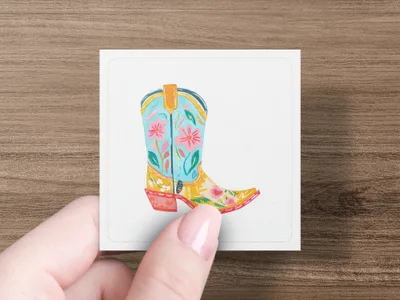 Colorful cowboy boot illustration with floral pattern on white card held by fingers.