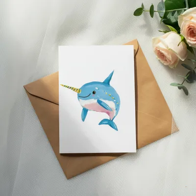Watercolor illustration of a smiling narwhal with a yellow and blue horn, on a card.