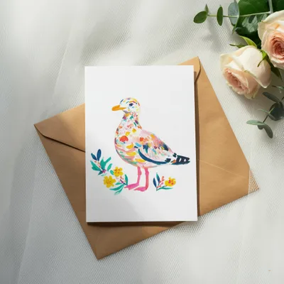 Watercolor card featuring a colorful seagull illustration with floral accents on a kraft envelope.