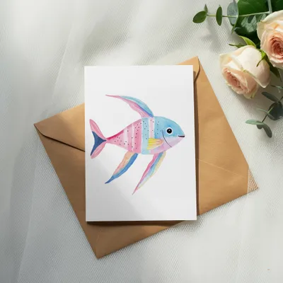 Watercolor painting of a colorful fish on a card atop a brown envelope.