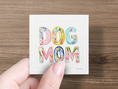 "Dog Mom" text with floral accents on a white square coaster.