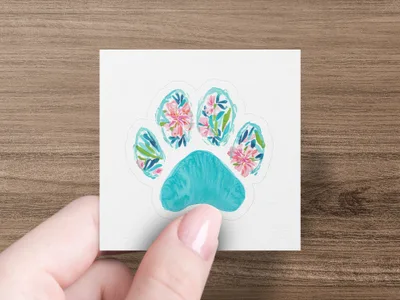 Turquoise paw print with floral watercolor design held by a hand.