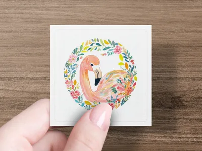 Watercolor flamingo with floral wreath, held in a hand.