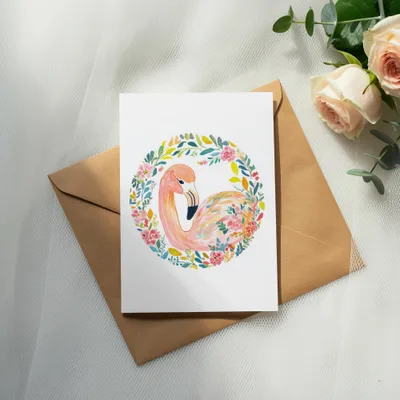 Watercolor flamingo in floral wreath on card atop envelope with roses.