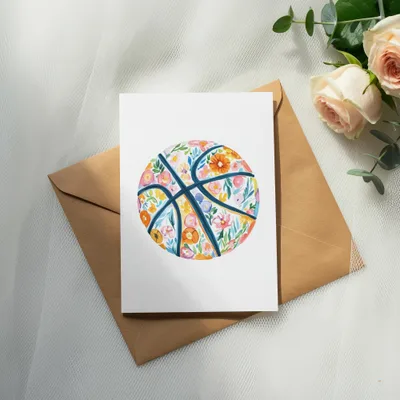 Floral basketball illustration on a card atop a brown envelope and roses.