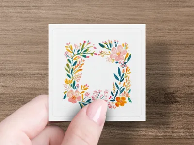 Square sticker with a floral wreath in watercolor, held by a hand.