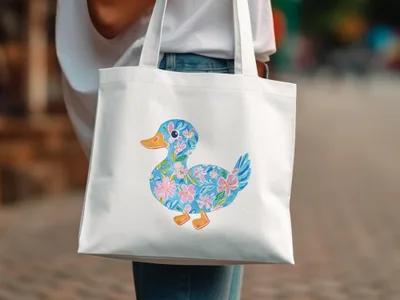 White tote bag with a cheerful blue duckling illustration adorned with pink flowers.