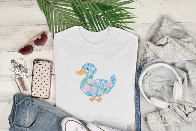 White t-shirt with a blue duck design adorned with pink and blue flowers.