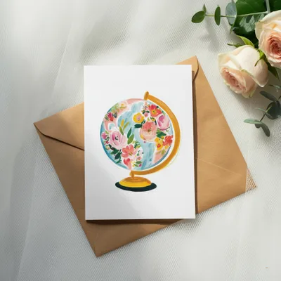 Watercolor globe with floral accents on a card in a kraft envelope.