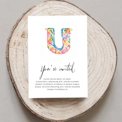 Watercolor "U" with floral accents on an invitation with "You're invited" text.