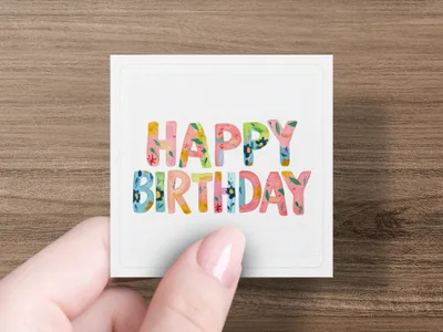 Hand holding square card with "Happy Birthday" in colorful floral lettering.