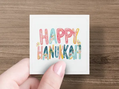 Hand holding card with "Happy Hanukkah" in colorful, stylized lettering.