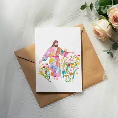 Watercolor painting of Jesus surrounded by colorful flowers on a brown envelope.