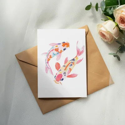 Two colorful koi fish watercolor painting on a card, resting on an envelope with roses.