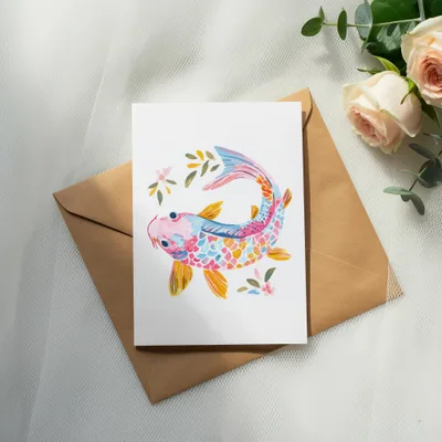 Watercolor koi fish illustration on a card atop a brown envelope with roses.