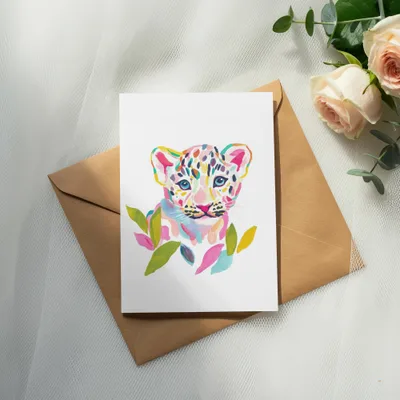 Watercolor painting of a colorful leopard cub on a card, resting on an envelope.
