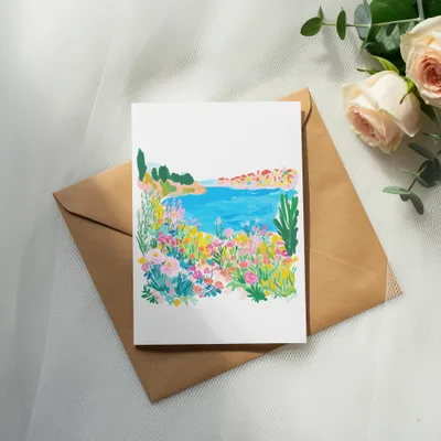 Watercolor painting of a coastal village with flowers and foliage on a brown envelope.