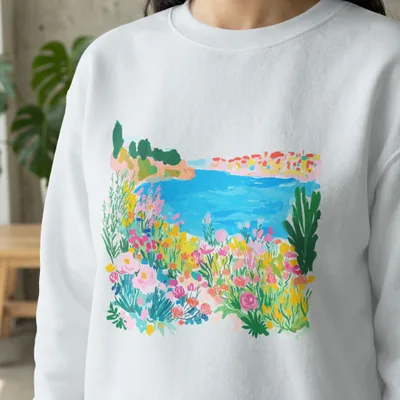 White sweatshirt with colorful floral and coastal landscape print.