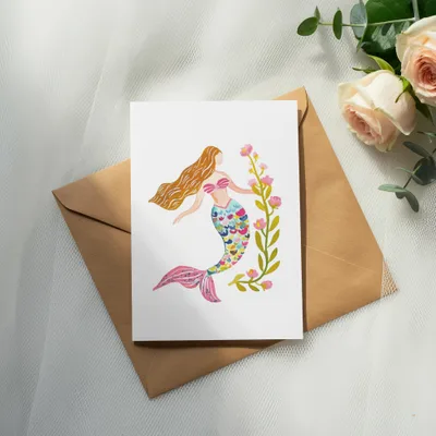Watercolor mermaid illustration on card with pink flowers and greenery.