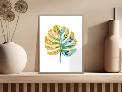 Colorful monstera leaf painting in a minimalist frame on a shelf.