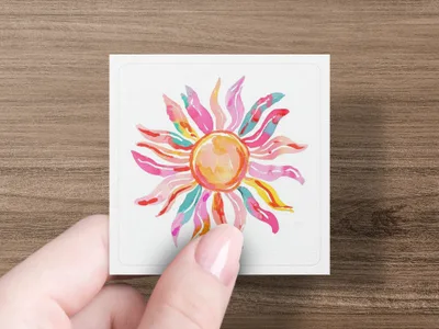 Pink and yellow watercolor sun on a white square held by a hand.