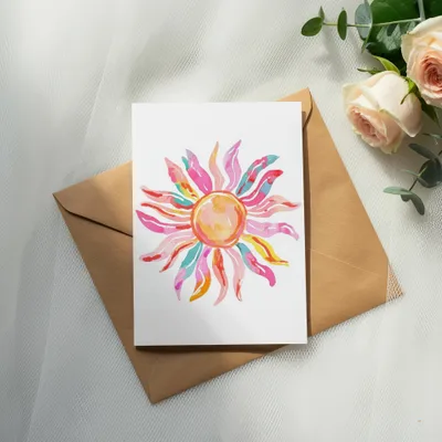 Watercolor sun art on a white card on a brown envelope.