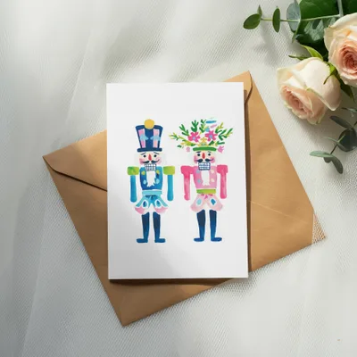 Two watercolor nutcracker figures, one with a hat, one with flowers, on a card.