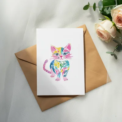 Colorful watercolor cat illustration on a white card, with a brown envelope and roses.