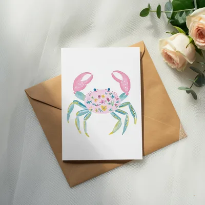 Card with a pink crab illustration featuring floral patterns on a brown envelope.