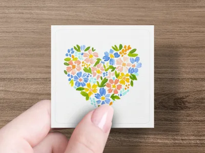Hand holding square card with colorful floral heart design.