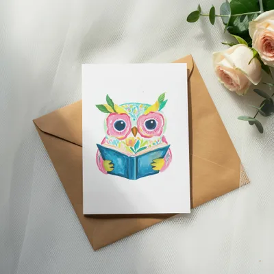 Watercolor owl reading a book on a brown envelope.