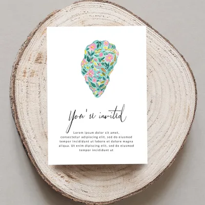 Invitation card with "You're invited" text and floral design on wood slice.