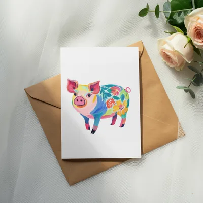 Watercolor illustration of a colorful, floral pig on a white card resting on an envelope.