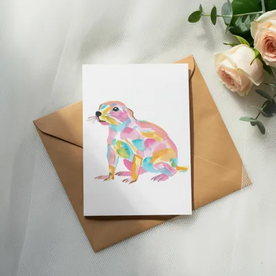 Watercolor illustration of a colorful prairie dog on a card, resting on a brown envelope.