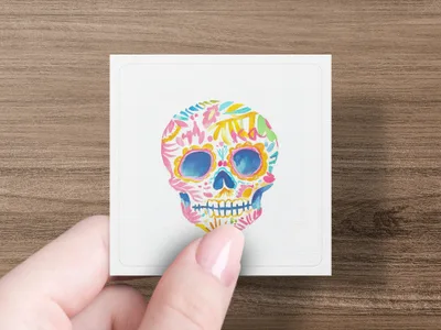 Square card with colorful floral sugar skull design held by fingers.