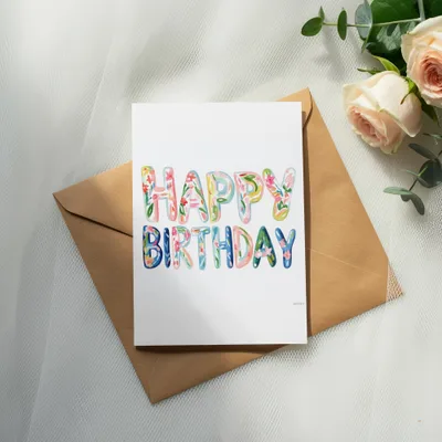 Watercolor "Happy Birthday" lettering on a card with a kraft envelope and roses.