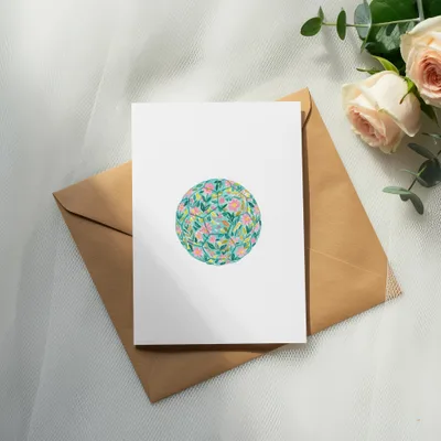 White card with floral circle design on brown envelope, roses nearby.