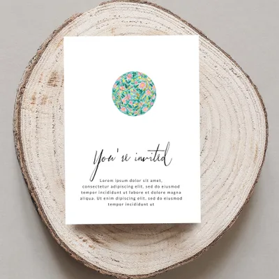 Invitation card with floral design and placeholder text, on a wood slice.