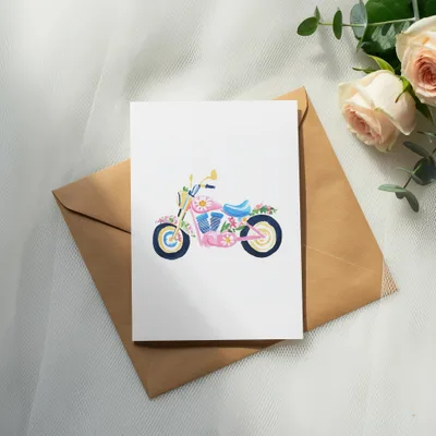 Pink motorcycle illustration with floral accents on a card, atop a brown envelope.