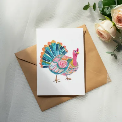 Colorful watercolor turkey on a card atop a brown envelope with roses.
