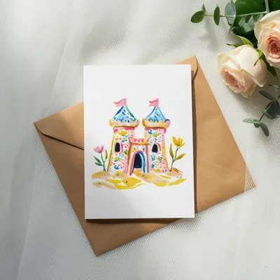 Watercolor sandcastle card with pink roses and eucalyptus on a brown envelope.