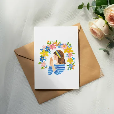 Card with woman in prayer surrounded by colorful flowers and Ukrainian flag colors.