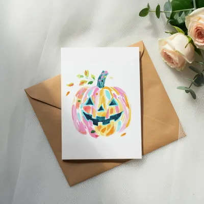 Watercolor Halloween pumpkin on card, next to roses and envelope.
