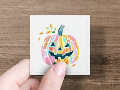 Colorful watercolor pumpkin with fall leaves on a card held by fingers.